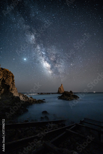 Vía láctea y estrellas del firmamento sobre el Arrecife de las Sirenas en el Cabo de Gata, Almeria, una noche de verano con el océano en el horizonte y las vías de desembarco en primer plano. photo