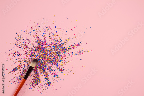 Brown professional cosmetic makeup brush with explosion of shiny colorful sparkles on bright pink background with copyspace for your text. Creative make-up concept