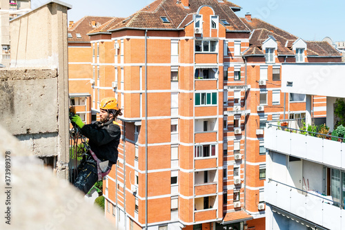 Male worker hanging on rope access and height construction project. Working on building wall insulation and facade painting decoration job. Tough and dangerous working environment