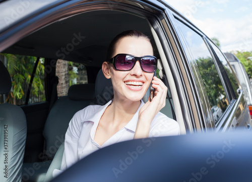 Happy young beautiful smiling woman talking on the phone sitting in her car. 