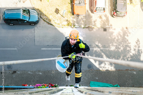 Male worker hanging on rope access and height construction project. Working on building wall insulation and facade painting decoration job. Thumbs up.