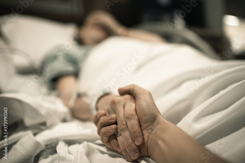 sick woman lying in hospital bed with friend holding her hand giving her support 