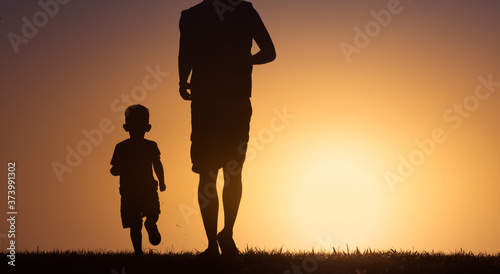 Father and son silhouette running playing outdoors in an open field. Parenting, and childhood concept. 
