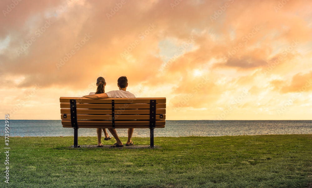 couple sitting on park bench watching the sunset. Love and relationships concept.  - obrazy, fototapety, plakaty 
