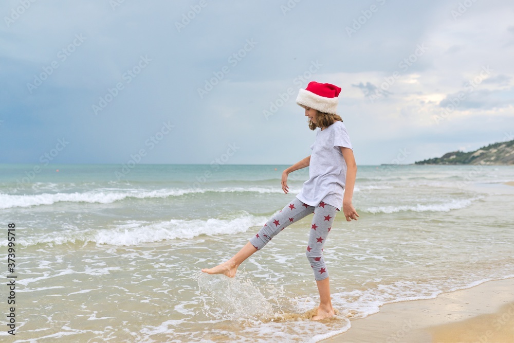 Background sea ocean beach, child girl in Santa hat having fun, back view