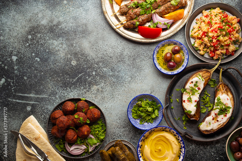 Middle eastern or Mediterranean dinner with grilled kebab  falafel  roasted and fresh vegetables  assorted Arabic meze and appetizers on rustic background table. Dinner table overhead  space for text 