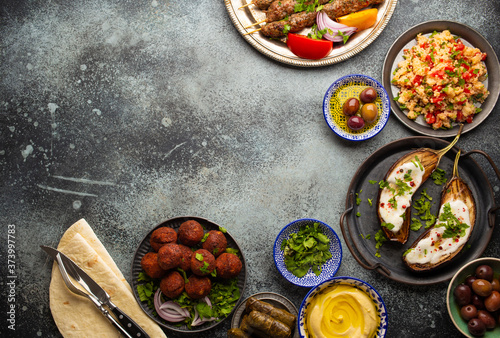 Middle eastern or Mediterranean dinner with grilled kebab, falafel, roasted and fresh vegetables, assorted Arabic meze and appetizers on rustic background table. Dinner table overhead, space for text
 photo