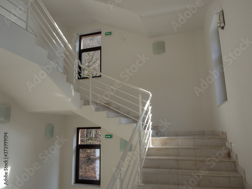 A stairwell with light steps with white railings and white walls and windows in dark frames photo