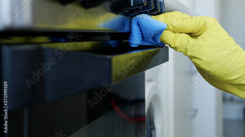 Closeup Image with Person Hands Wearing Protective Yellow Household Gloves in the Kitchen and Cleaning a Stove