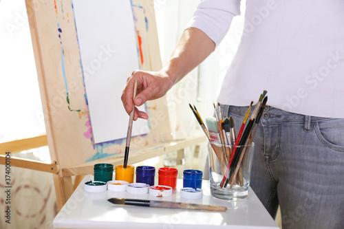 the artist's hand holds a brush on the background of the easel