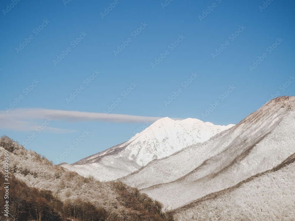 Mountain peaks illuminated by sunbeams with a snowy forest in the foreground against a clear sky background Mountain peaks illuminated by sunbeams with a snowy forest in the foreground against a clear sky background