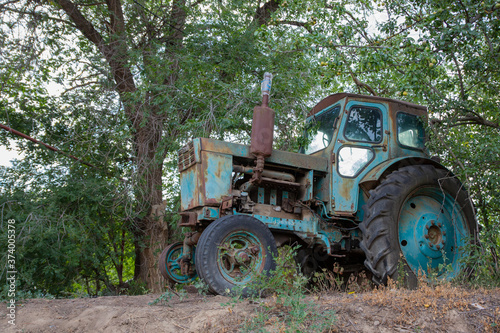 Vintage photo - an old blue tractor standing under a green branching tree