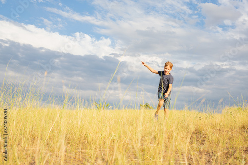A cheerful, happy child runs through a summer field with yellow grasses against a blue cloudy sky.