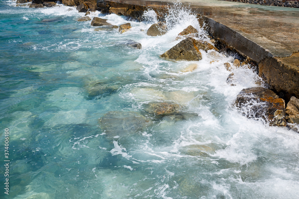 Wonderful views of the blue Mediterranean Sea. Sunny rocks, waves with foam and splashing water. The wave crashes into the rocks on the shore Wonderful views of the blue Mediterranean Sea. Sunny rocks, waves with foam and splashing water. The wave crashes into the rocks on the shore