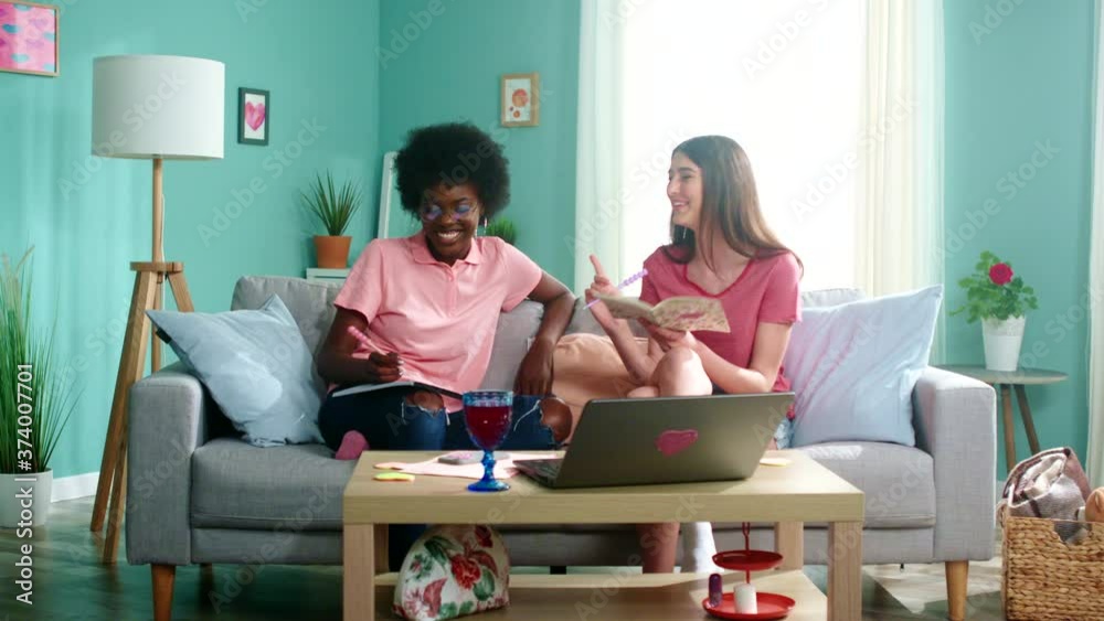 Two young women, mixed race students, stay home studying together, make notes and talk, have fun together, laughing, enjoying their friendship, Slow motion. Two young women, mixed race students, stay home studying together, make notes and talk, have fun together, laughing, enjoying their friendship, Slow motion.