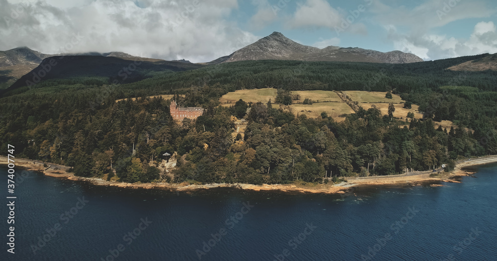 Scotland, Brodick ocean bay aerial view: alone sailboat at Firth-of-Clyde Gulf water against Scottish nature landscape. Beautiful mountains at horizon with wide woods. Panorama scenery shot