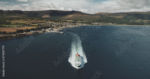 Scotland ocean, passenger ferry aerial view in coastal water of Firth-of-Clyde Gulf. Ship crossing from Brodick terminal to Scottish mainland. Cityscape at green valleys. Cinematic shot photo