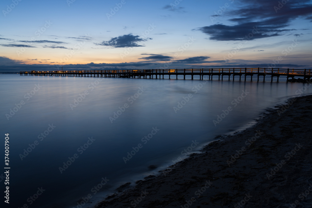Long wooden jetty over sea during summer sunset with reflection in the water. Captured in south Sweden.