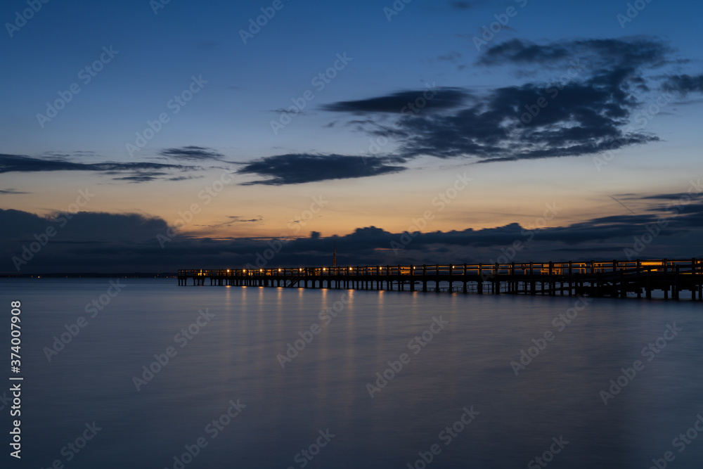 Long wooden jetty over sea during summer sunset with reflection in the water. Captured in south Sweden.