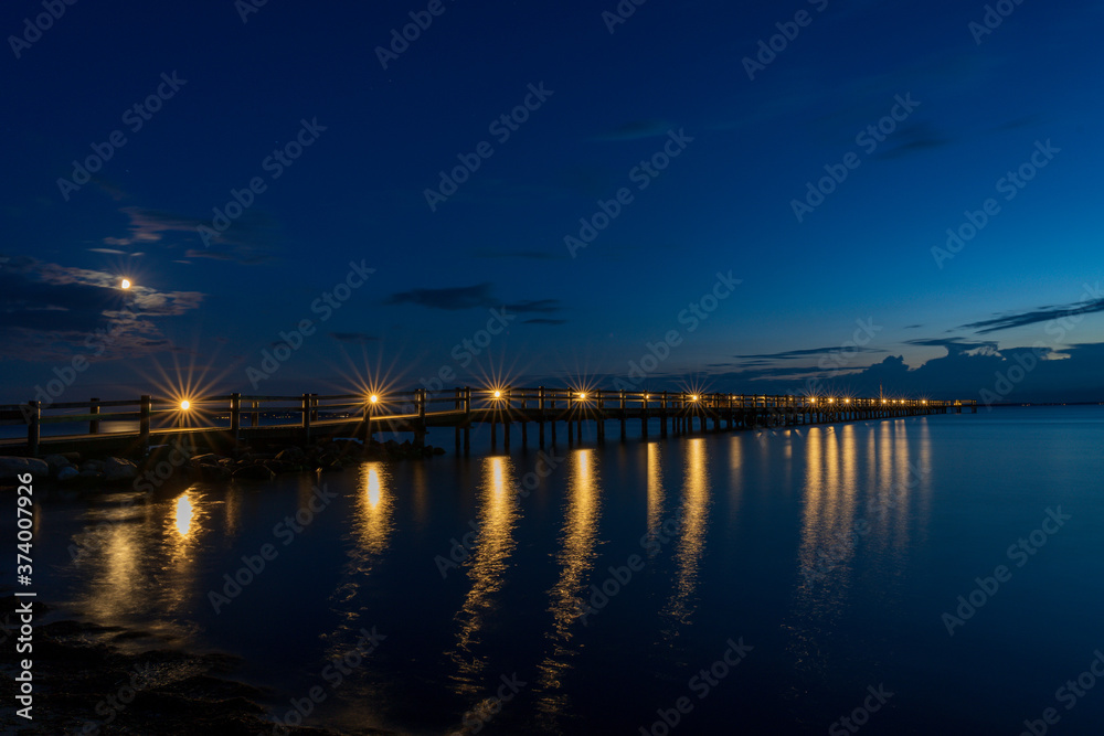 Long wooden jetty over sea during summer sunset with reflection in the water. Captured in south Sweden.