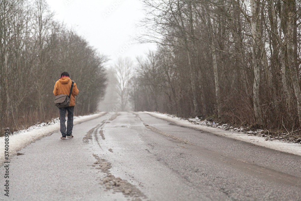 Lonely man in orange jacket walks along empty road in winter forest