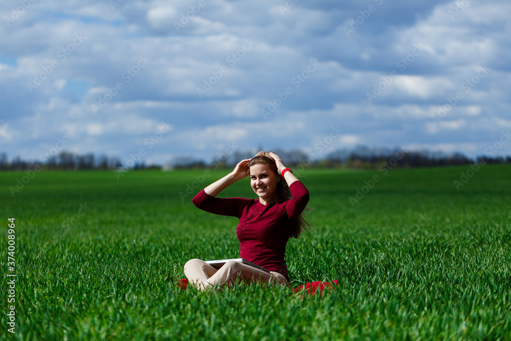 Young successful woman is sitting on green grass with a laptop in her hands. Rest after a good working day. Work on the nature. Student girl working in a secluded place. Workplace in nature Young successful woman is sitting on green grass with a laptop in her hands. Rest after a good working day. Work on the nature. Student girl working in a secluded place. Workplace in nature