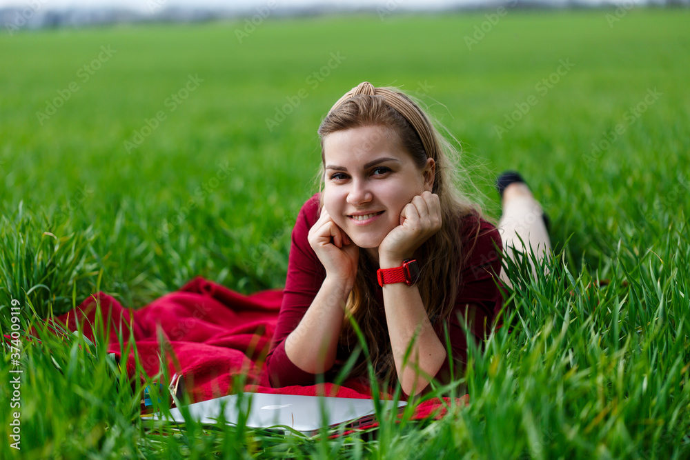 Young beautiful woman student with a laptop lies on the grass. Work outdoors. Young beautiful woman student with a laptop lies on the grass. Work outdoors.