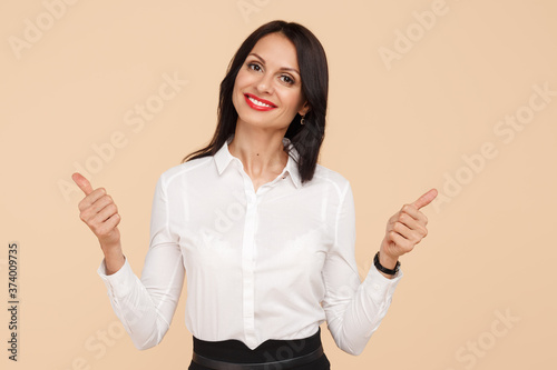 Positive young modern business woman showing thums up over beige background. Success and winner concept. photo