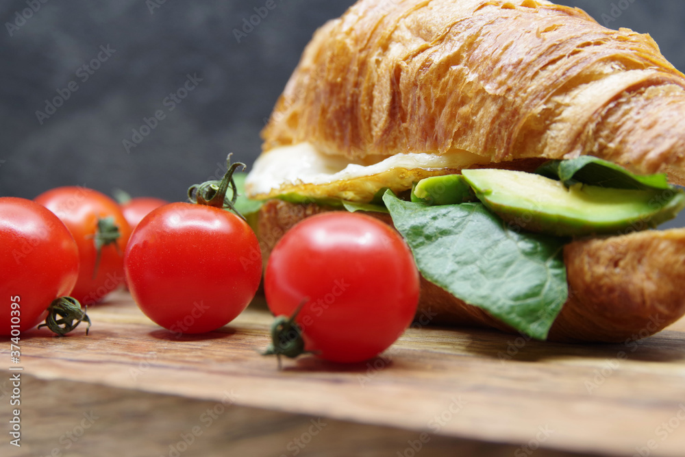 Croissant stuffed fried egg and avocado on a wooden tray Croissant stuffed fried egg and avocado on a wooden tray
