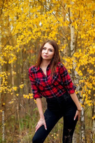 Portrait of pretty young woman of Slavic appearance in dark casual clothing in autumn, stand in forest with trees. Cute model walks in Park in golden autumn against background of nature and road