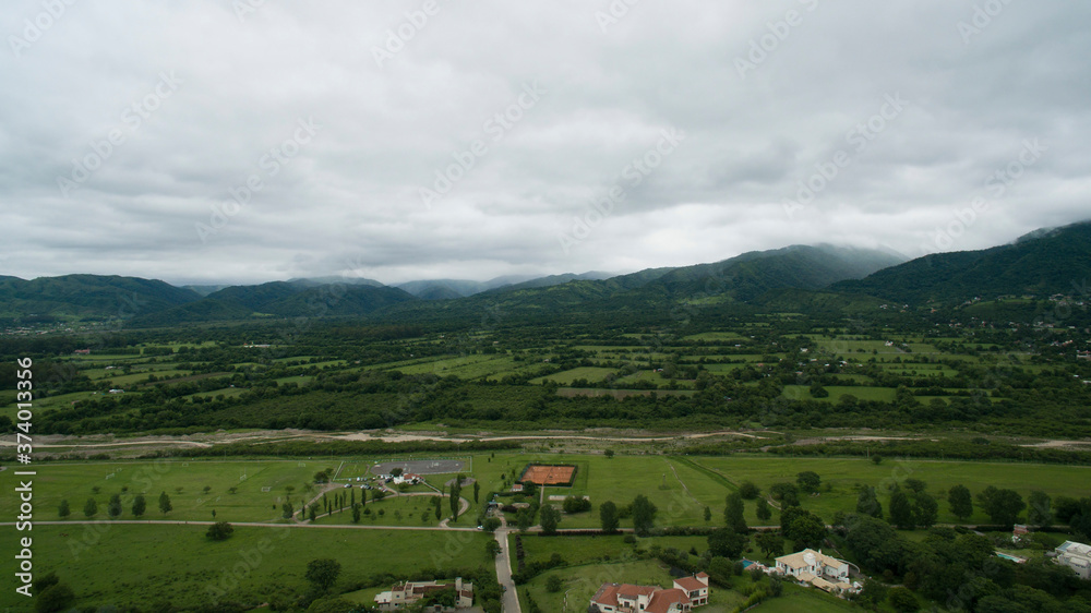 Countryside landscape at nightfall. Aerial view of the green field, farmland, forest, hills, and houses, under a cloudy sky. 