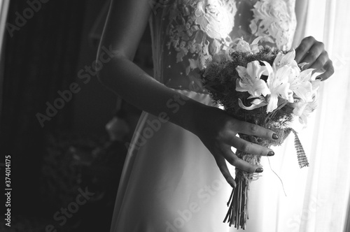 Novia en blanco y negro con ramo en la mano junto a ventana con luz natural