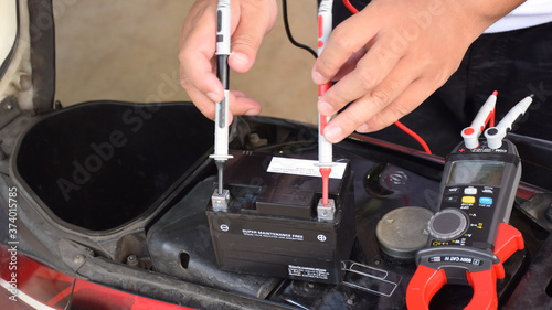 A mechanic is measuring the voltage of a motorcycle battery with clamp meter for maintenance. Thai text is mean "Charging Method"
