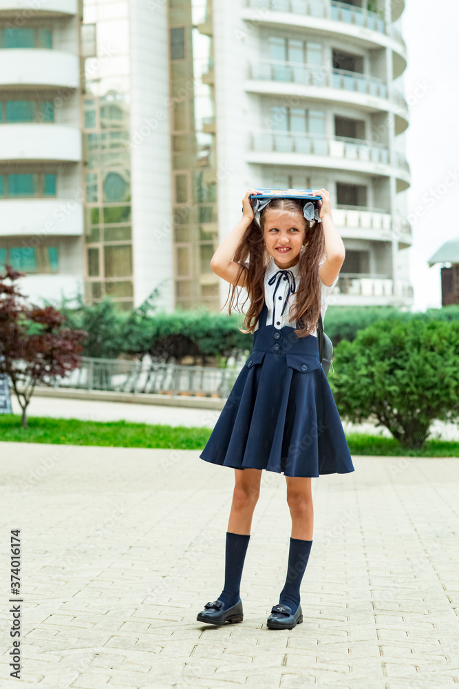 a beautiful girl, in a blue school uniform, with a school backpack, near the school building. Return to school, September 1