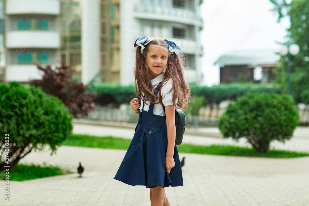 a beautiful girl, in a blue school uniform, with a school backpack, near the school building. Return to school, September 1