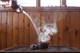 in a traditional chinese clay teapot for making tea, water is poured with a cloud of steam on a wooden background