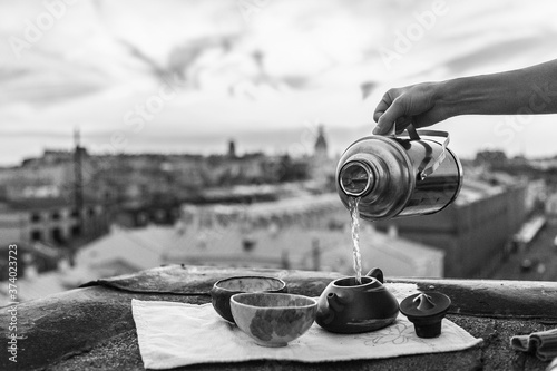 Hands pouring chinese tea into a clay teapot overlooking the sunset city