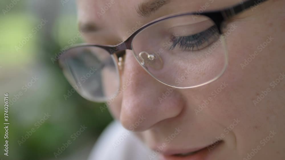 attractive young woman wearing stylish eyeglasses looks at something smiling on green blurred background extreme close view attractive young woman wearing stylish eyeglasses looks at something smiling on green blurred background extreme close view