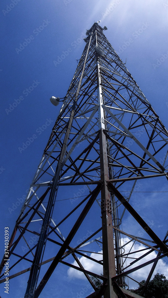 Tall metal tower with bouncing signal antennas, seen from the surface, with blue sky in the background and few clouds Tall metal tower with bouncing signal antennas, seen from the surface, with blue sky in the background and few clouds