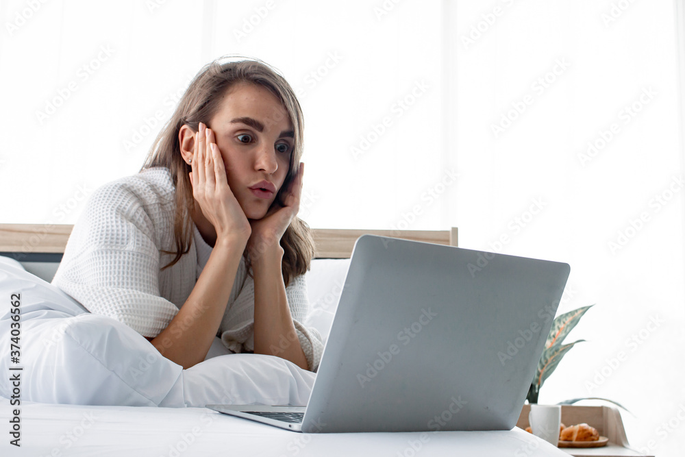 Caucasian woman is shocked after playing laptop on white bed. Caucasian woman is shocked after playing laptop on white bed.