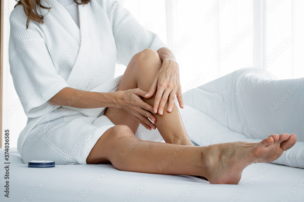 Woman applying body cream on her leg on white bed. Woman applying body cream on her leg on white bed.