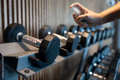 Hand of asian woman is spraying alcohol on the handle of the dumbbell to clean it,prevent Coronavirus infection,safety of the COVID-19 outbreak,people is cleaning the dumbbells in the gym or fitness