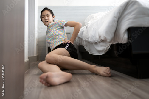 Asian child girl was sitting in pain on the floor after she fell out of bed while sleeping,injured,sad woman holding hip with her hand,suffering from pain after sleepwalk,problem of parasomnia disease