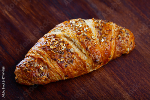 One multigrain croissant sprinkled with seeds of brown and gold flax on wooden background