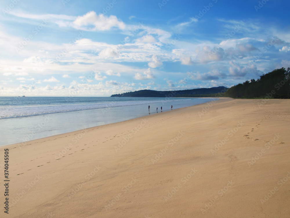 Family rests on the beach. Sea view, clean sand, few people. Beautiful panorama. Green forest and hills in a distance. Father, mother, son, daughter walking along the water. Waves, sky, white clouds.