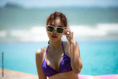 Asian sexy woman in bikini swimwear sitting and lying on edge of swimming pool and looking on the beach/Summer holiday vacation © Somchai