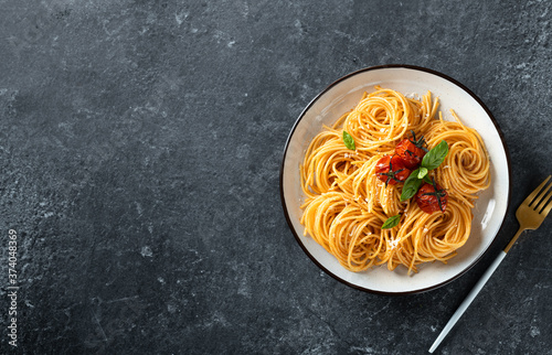 pasta with cherry tomatoes in a white plate on a dark background, italian food. Top view, copy space