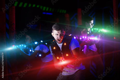 Portrait of guy in colored beams of laser guns during laser tag game on dark arena © JackF