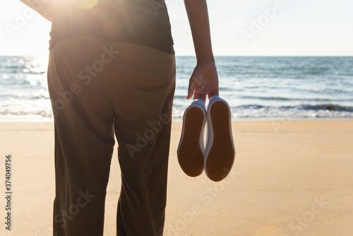 Fototapeta Naklejka Na Ścianę i Meble -  Woman hands holding shoes at the beach during sunset time,Back view
