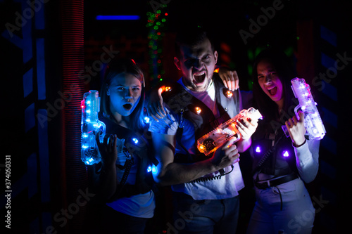 Group portrait of young people with laser guns having fun on dark lasertag arena